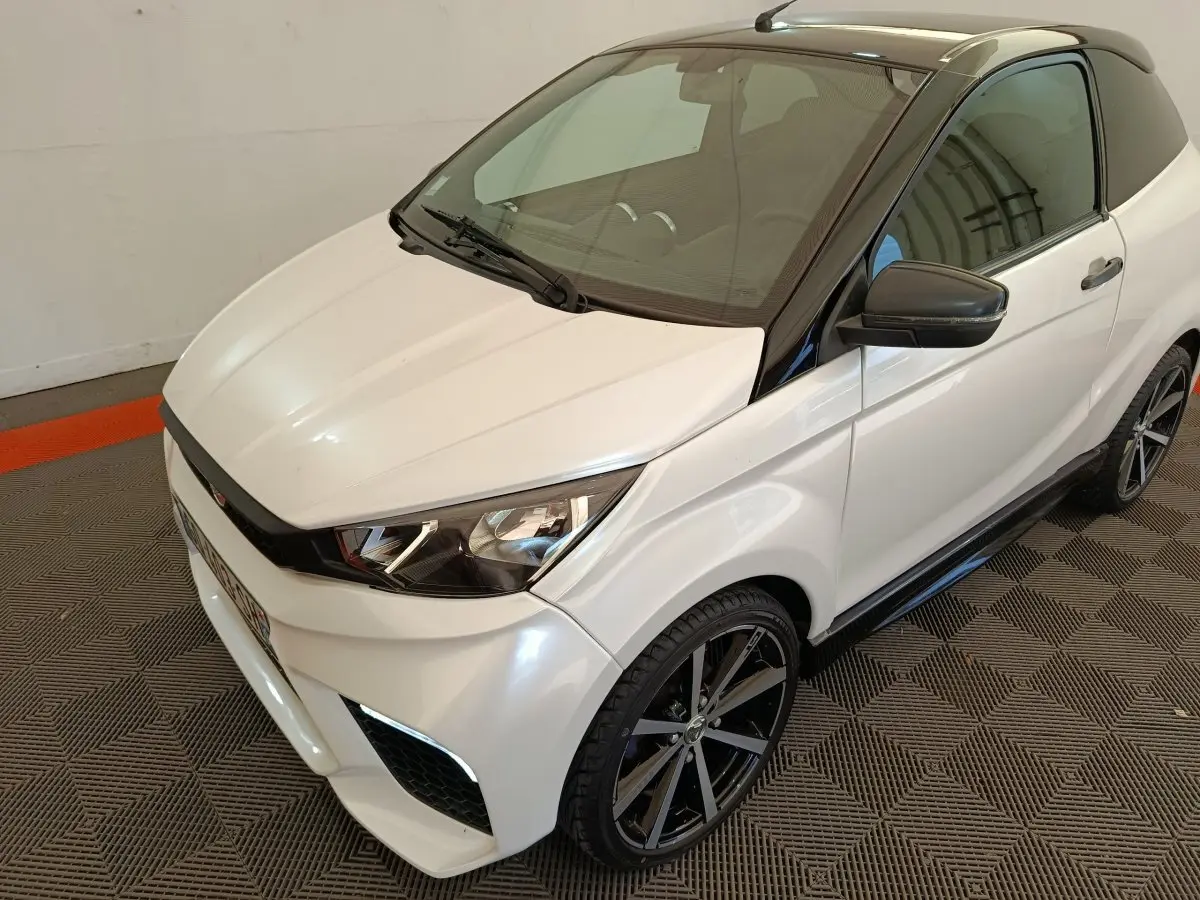 Vue 3/4 avant droite de l'AIXAM Ambition 0.5 City Coupe GTI blanche avec toit noir et rétroviseur droit noir.