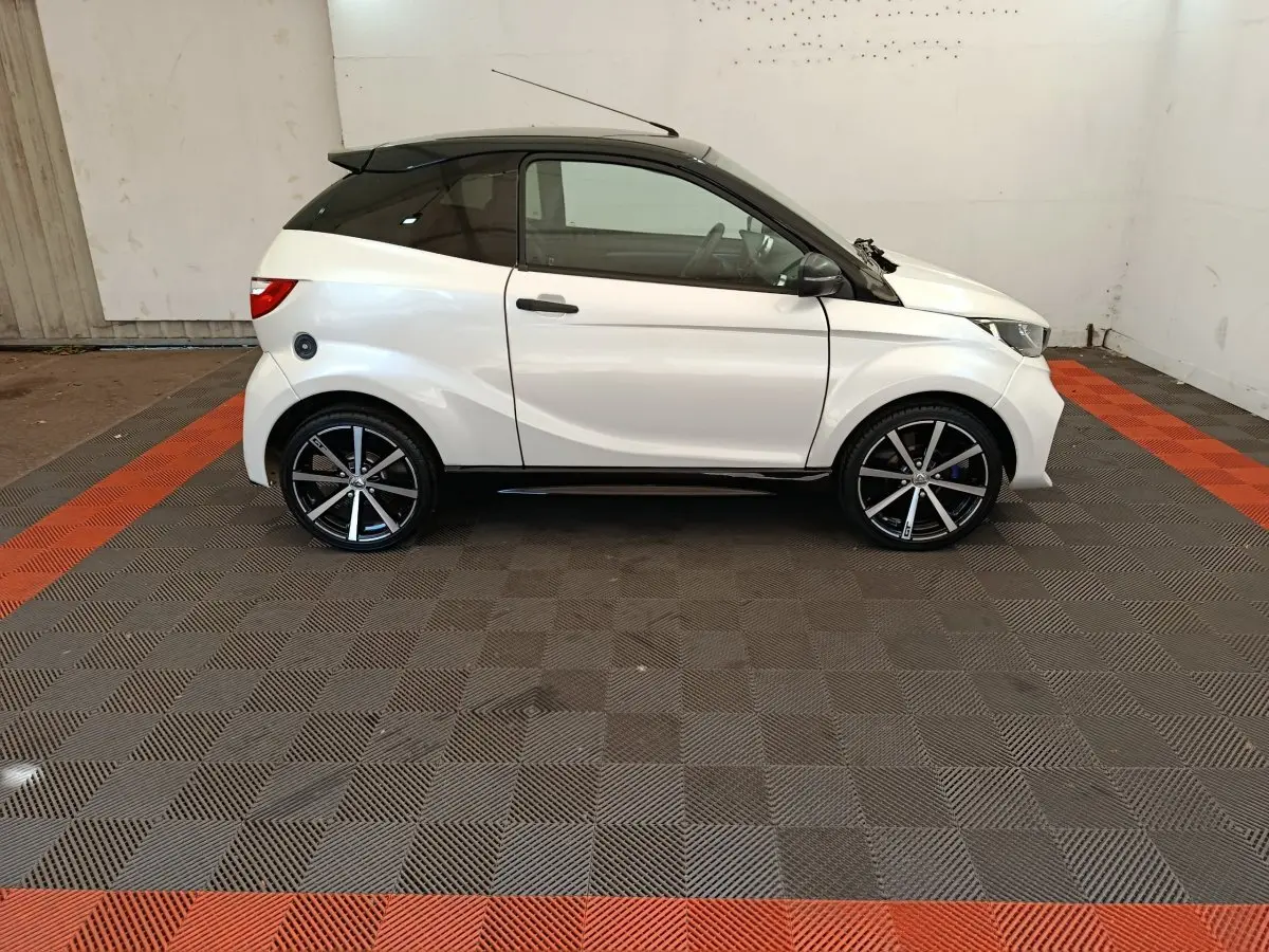 Vue de profil côté gauche d'une Aixam Ambition 0.5 City Coupe GTI blanche avec toit noir et jantes noires.