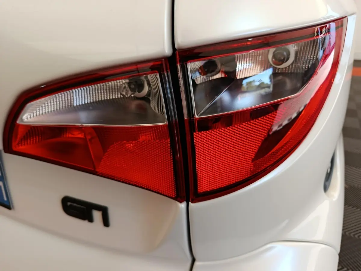 Gros plan sur les feux arrière rouges et blancs d'une Aixam Ambition 0.5 City Coupe GTI blanche, avec logo GT visible.