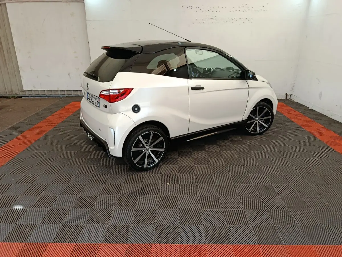Vue 3/4 arrière droite de l'AIXAM Ambition 0.5 City Coupe GTI blanche avec toit noir et jantes noires.
