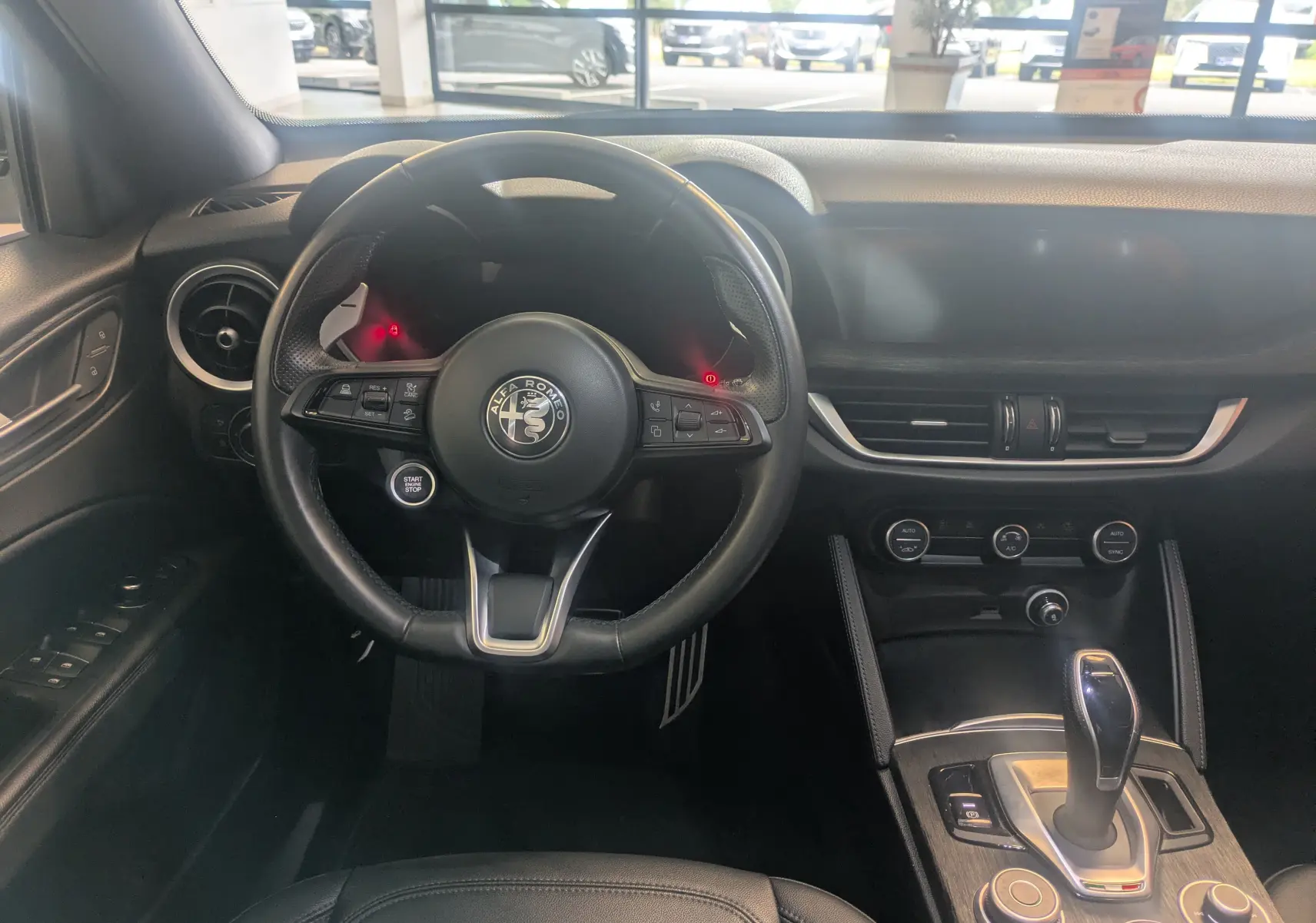 Vue intérieure centrée sur le volant cuir noir et la console centrale d'une Alfa Romeo Stelvio blanche 2023.