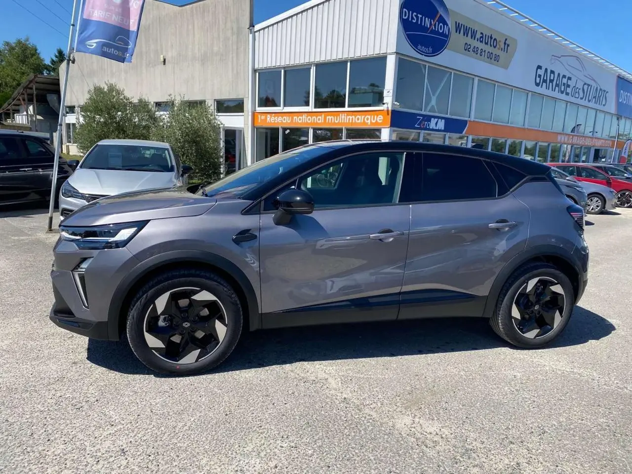 Profil côté gauche du Renault Captur 2025 gris Cassiopée avec toit noir et jantes aluminium noires sur parking.
