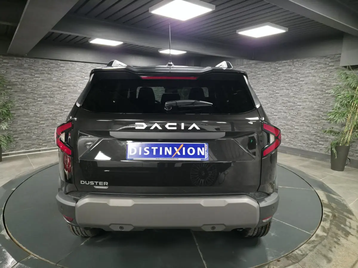 Vue arrière d'un Dacia Duster noir nacré 2025 avec logo DACIA lumineux et pare-chocs gris dans un showroom.