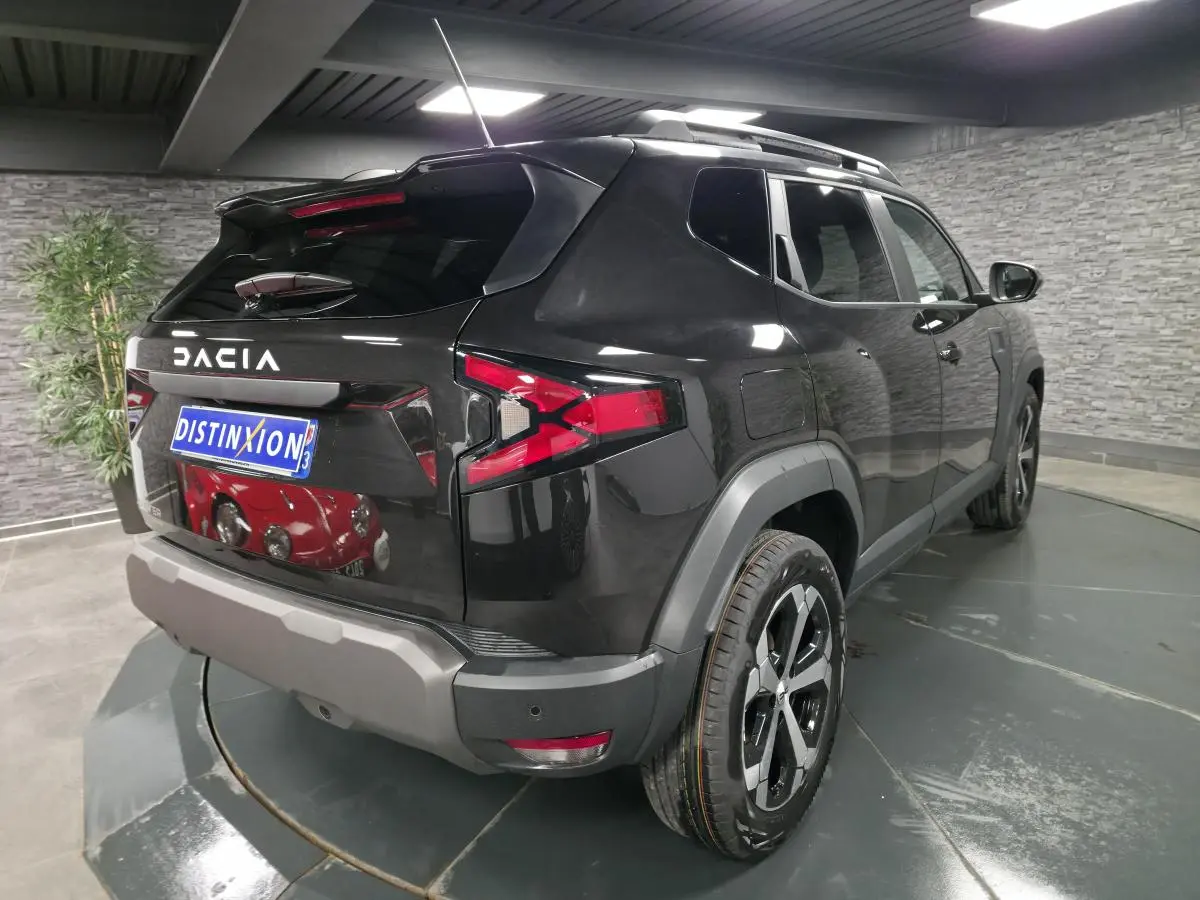Vue 3/4 arrière droite du Dacia Duster 1.6 Hybrid noir nacré avec barres de toit et jantes alliage 18 pouces.