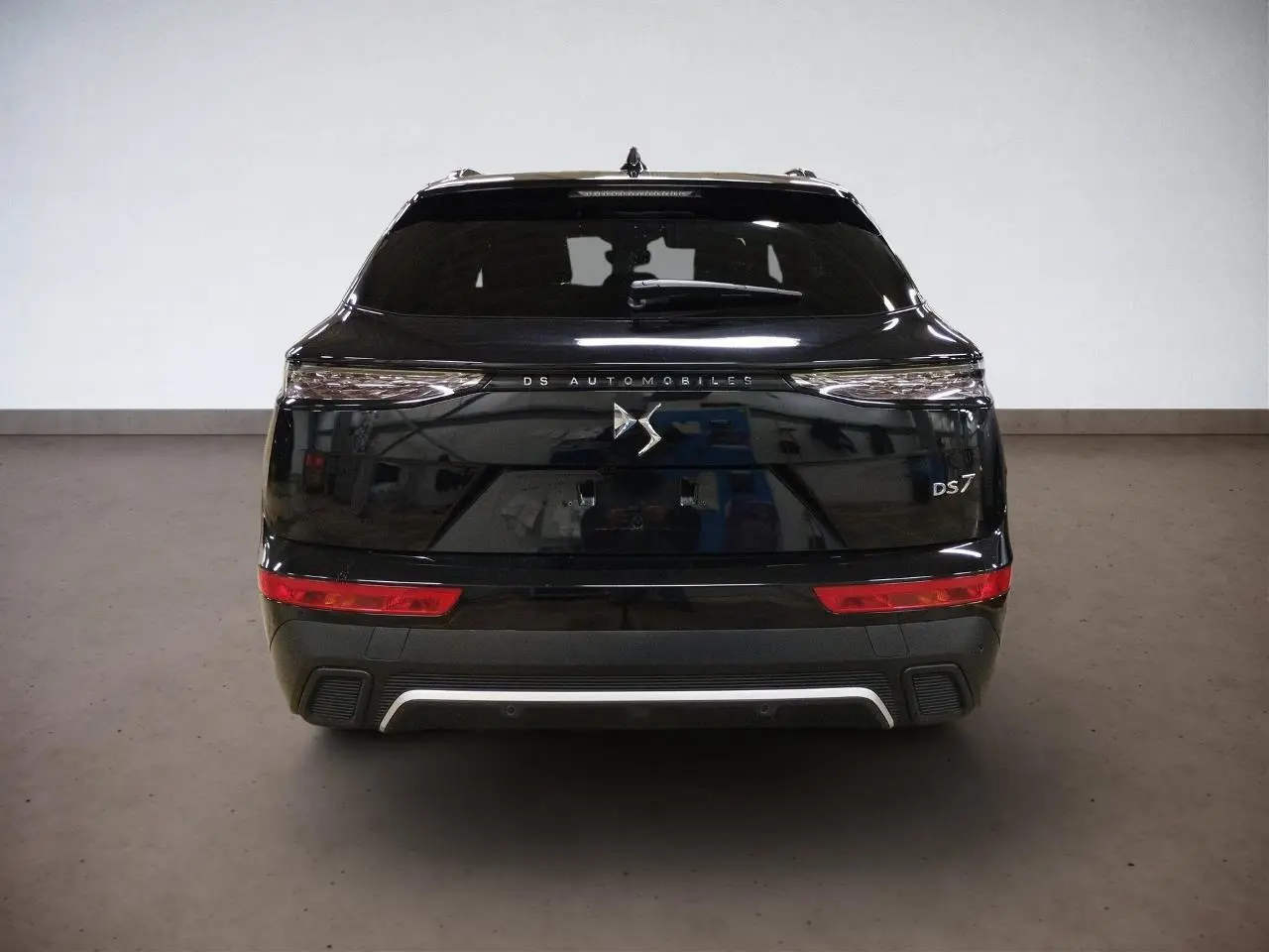 Vue arrière du DS7 noir Perla avec feux arrière 3D et logo DS centré sur le hayon dans un intérieur neutre.