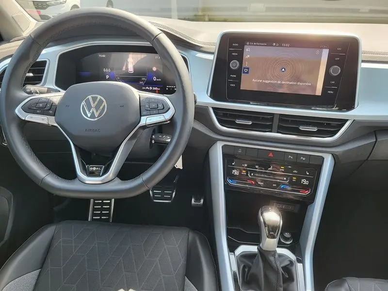 Vue intérieure frontale du tableau de bord et volant noir du Volkswagen T-Roc gris Indium avec écran tactile et commandes digitales.
