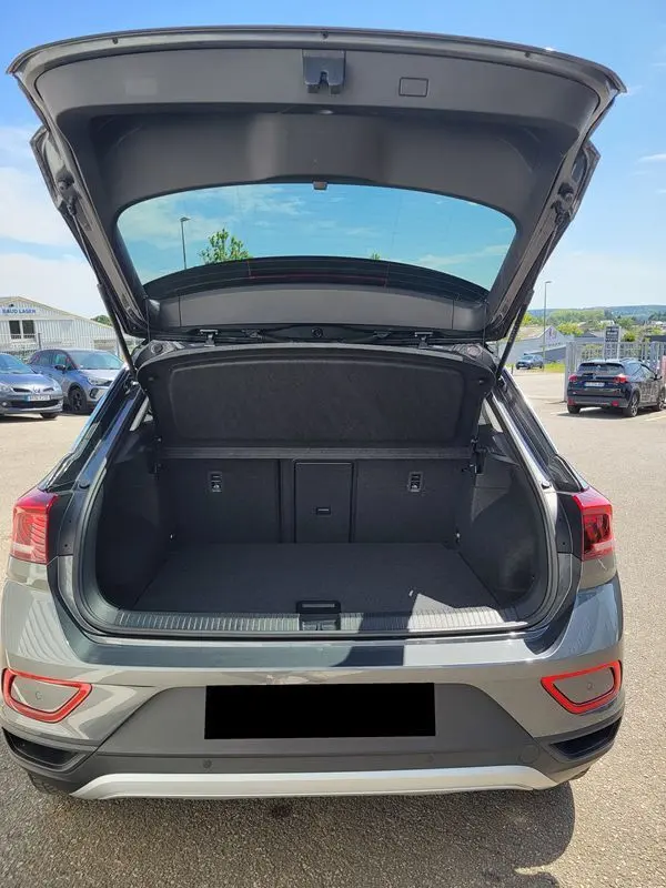 Vue arrière du Volkswagen T-Roc gris Indium 2025 avec coffre ouvert et intérieur spacieux visible en extérieur.