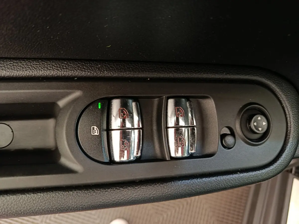 Gros plan sur les commandes chromées des lève-vitres et réglages des rétroviseurs côté conducteur d'une MINI Countryman noire.