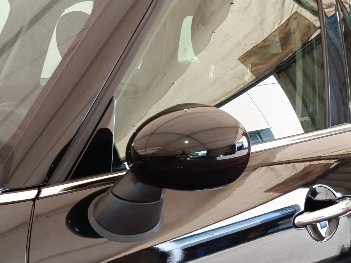 Gros plan sur le rétroviseur côté gauche noir brillant d’un MINI Countryman Cooper 2019 noir, avec reflet de l’environnement.