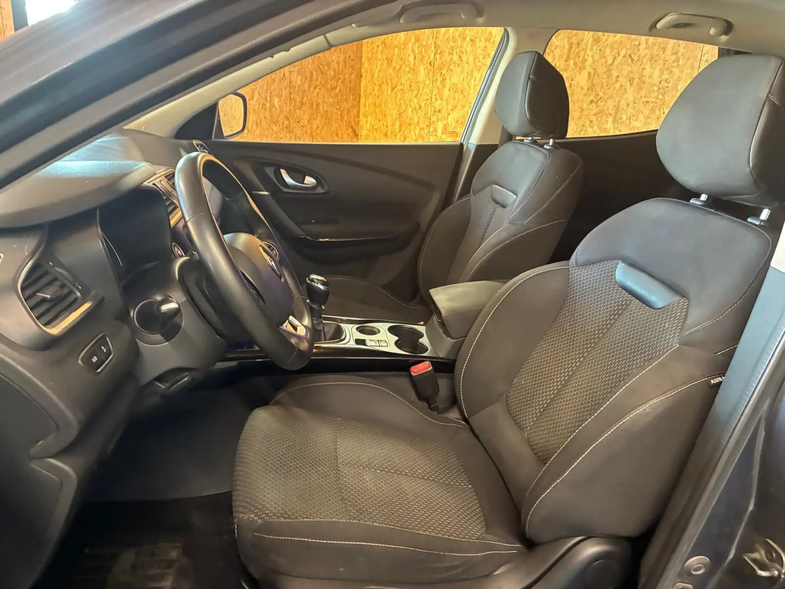 Vue intérieure côté conducteur du Renault Kadjar gris 2019, sièges tissu noir et volant avec boîte manuelle.