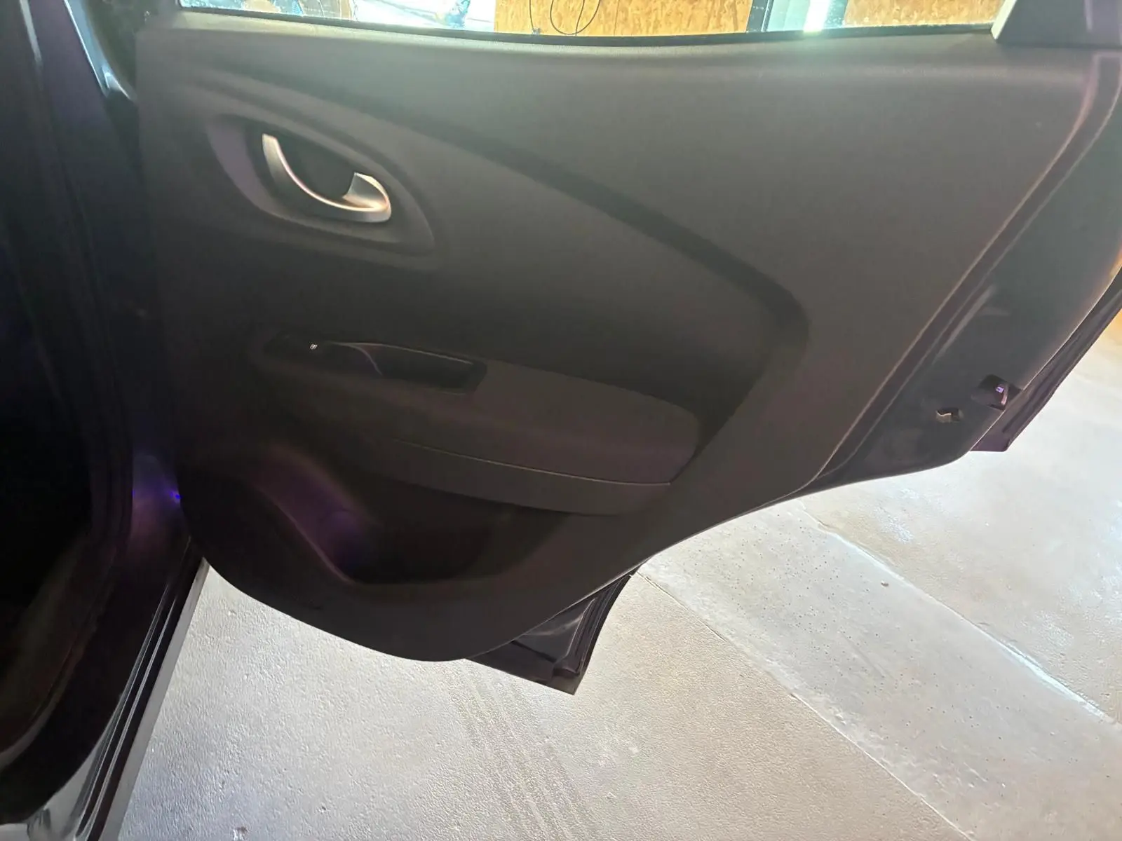 Vue intérieure de la porte arrière droite du Renault Kadjar gris, montrant la poignée et le panneau de porte en tissu noir.