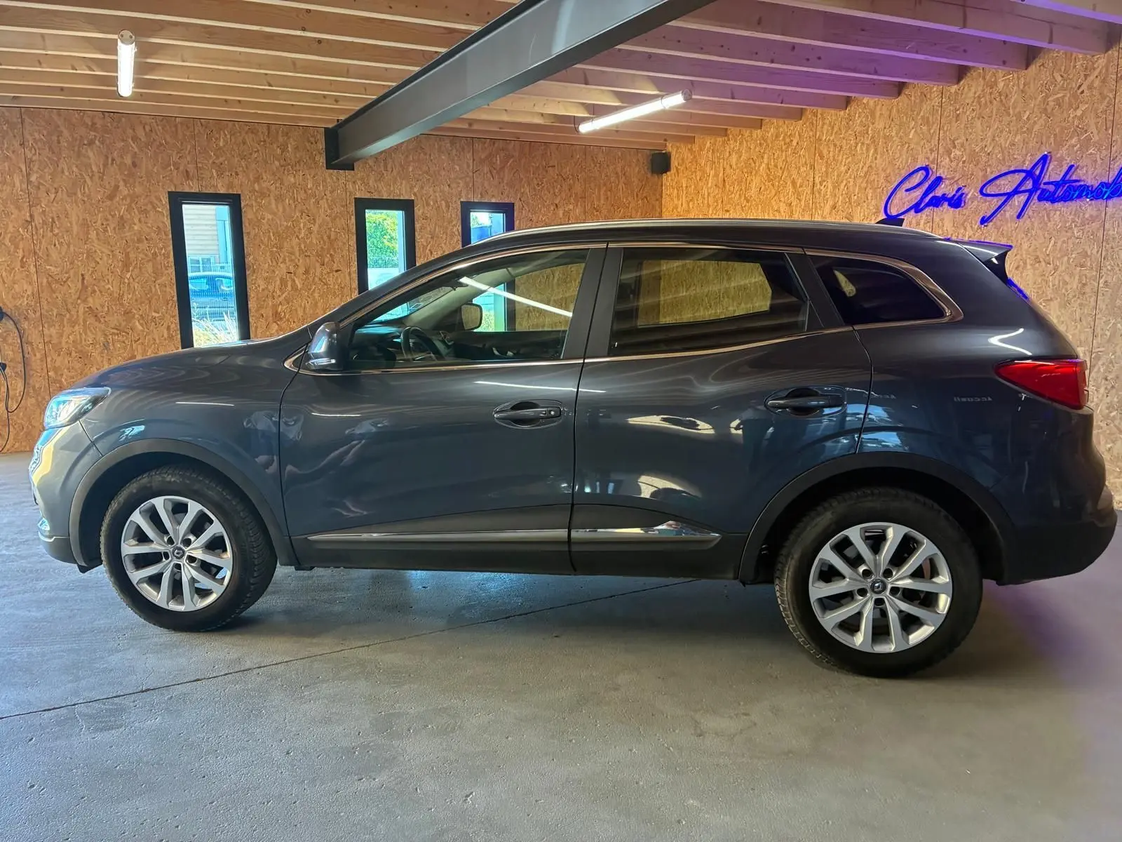Profil côté gauche d'un Renault Kadjar gris 2019 stationné en intérieur, avec jantes alliage et vitres teintées.