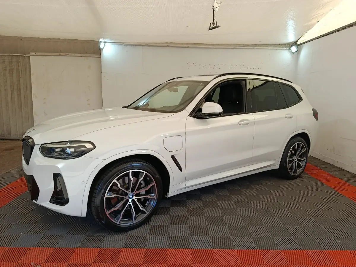 BMW X3 xDrive30e blanc en 3/4 avant droit, avec jantes alliage et prises de recharge latérales visibles.