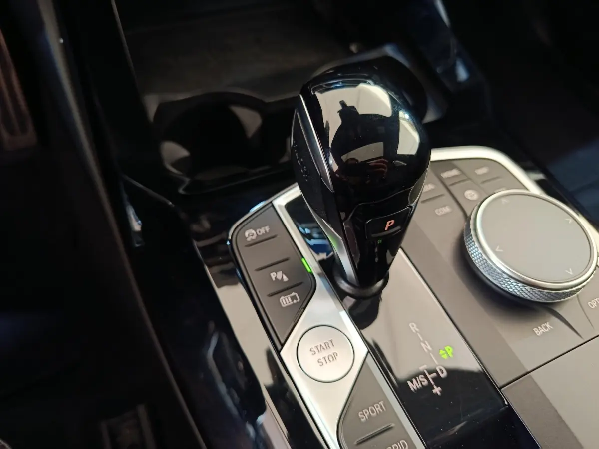 Gros plan sur la commande de boîte automatique noire et les boutons de contrôle du BMW X3 xDrive30e blanc.