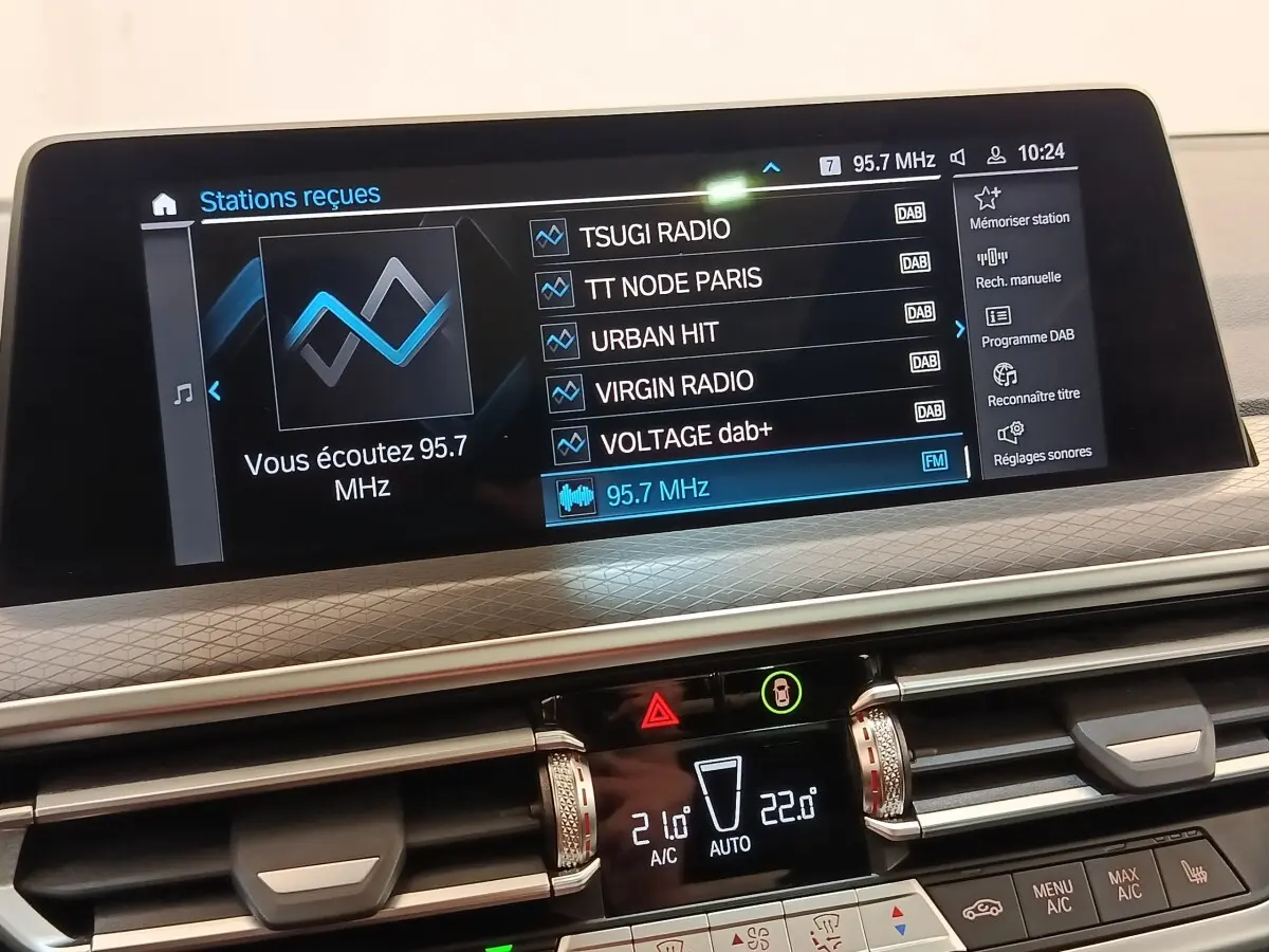 Affichage tactile central du tableau de bord du BMW X3 blanc, montrant les réglages radio et climatisation.