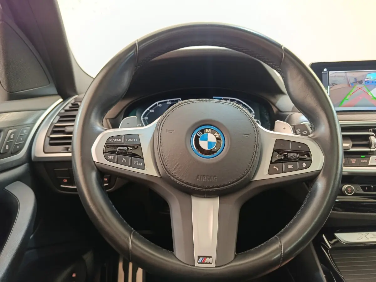 Vue rapprochée du volant cuir noir BMW X3 xDrive30e 2023 avec commandes multifonctions et logo M Sport.