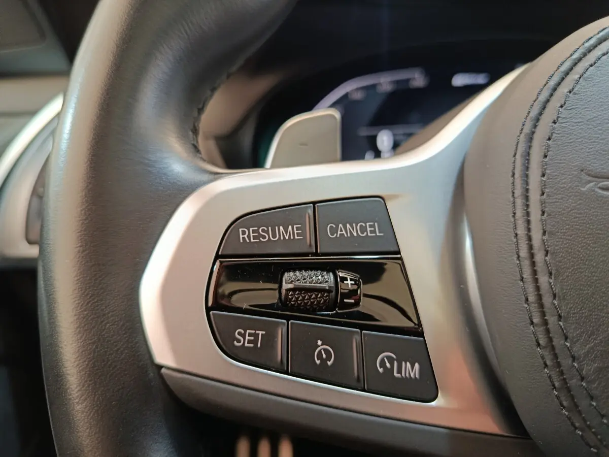 Gros plan sur les commandes de régulateur de vitesse au volant cuir d'une BMW X3 blanc, version 2023.