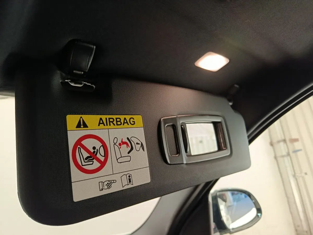 Pare-soleil intérieur noir avec miroir intégré et étiquette d'avertissement airbag, côté conducteur BMW X3 blanc visible au rétro.