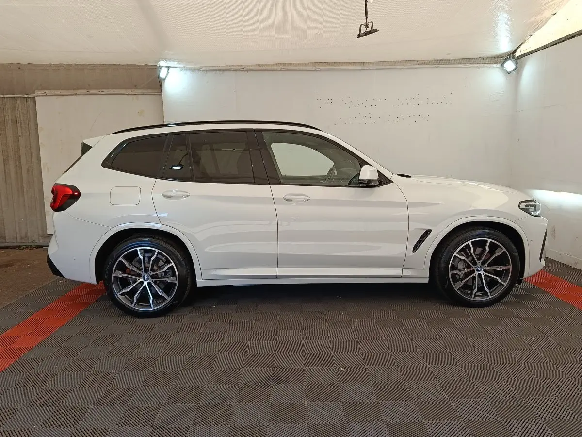BMW X3 xDrive30e blanc vue de profil côté gauche dans un garage avec jantes alliage et toit noir.