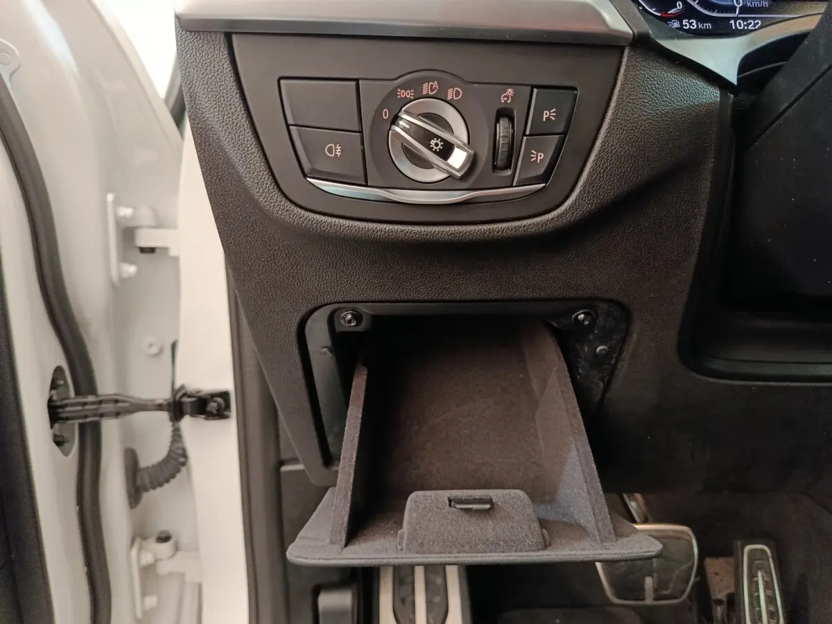 Détail intérieur côté gauche de la BMW X3 xDrive30e 2023, avec commande des phares et rangement ouvert.