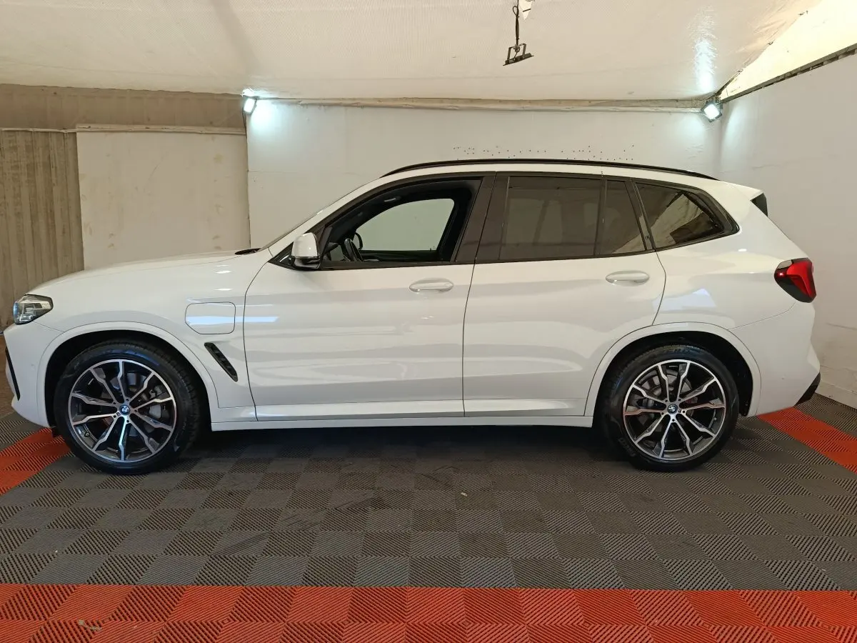 BMW X3 xDrive30e blanc en vue profil côté gauche, avec jantes alliage et prise de recharge visible.