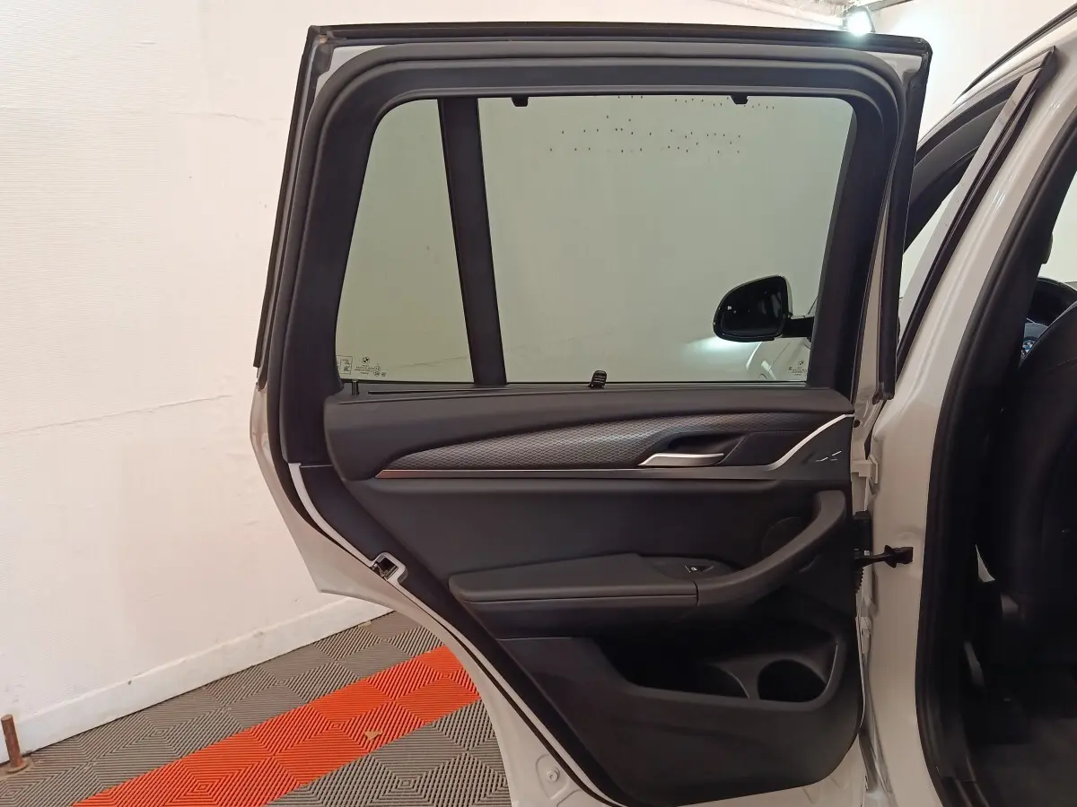 Vue intérieure de la porte arrière droite ouverte d'un BMW X3 blanc, avec garniture noire et détails argentés.