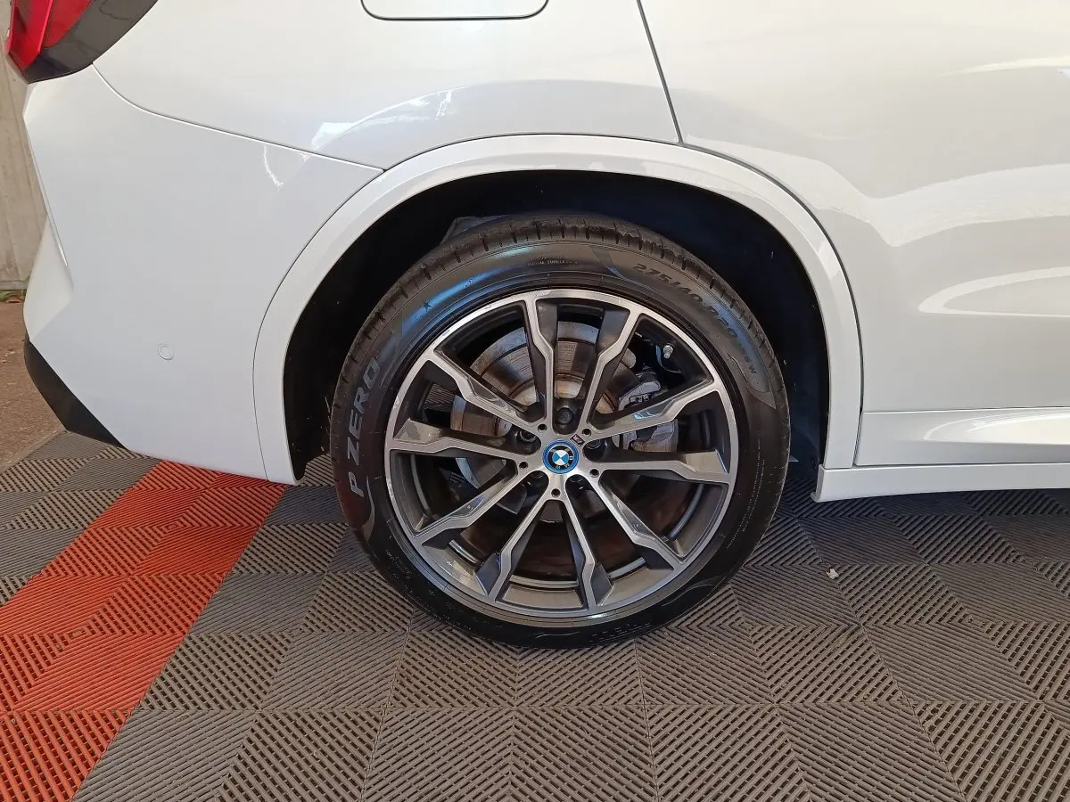 Gros plan sur la roue arrière droite d’un BMW X3 blanc, mettant en valeur la jante alliage M Sport et le pneu Pirelli P Zero.