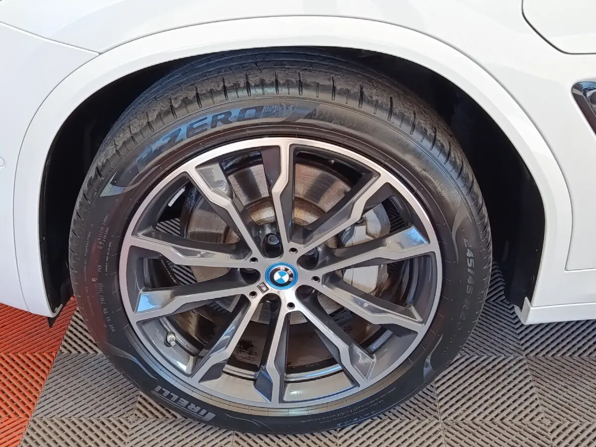 Gros plan sur la roue avant droite du BMW X3 blanc, jante alliage sombre à design sportif et pneu Pirelli P Zero.