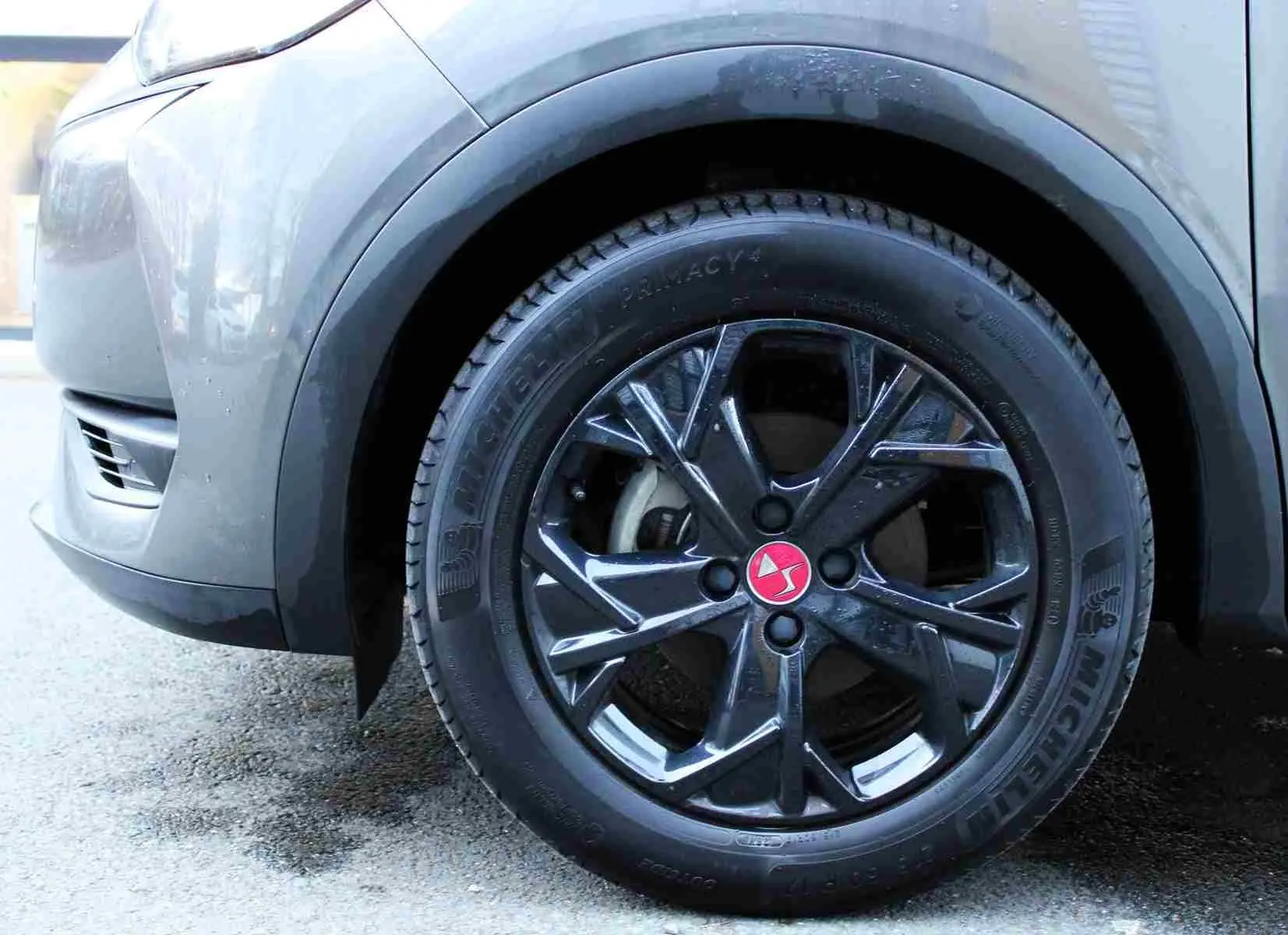 Gros plan sur la roue avant gauche du DS3 Crossback gris platinium, jante noire brillante avec logo rouge DS au centre.