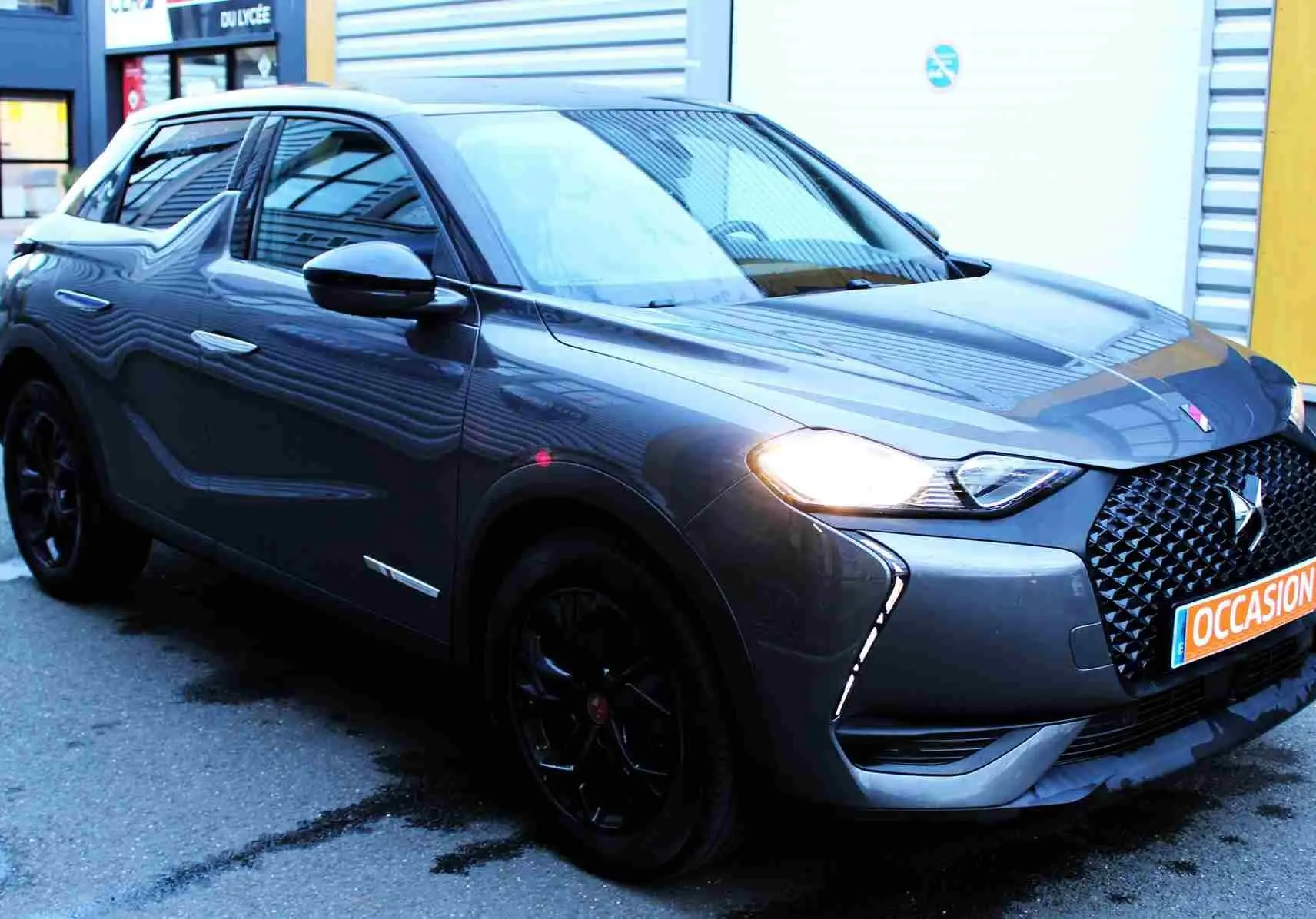 Vue 3/4 avant gauche d'un DS3 Crossback gris platinium métallisé avec calandre noire et feux allumés.