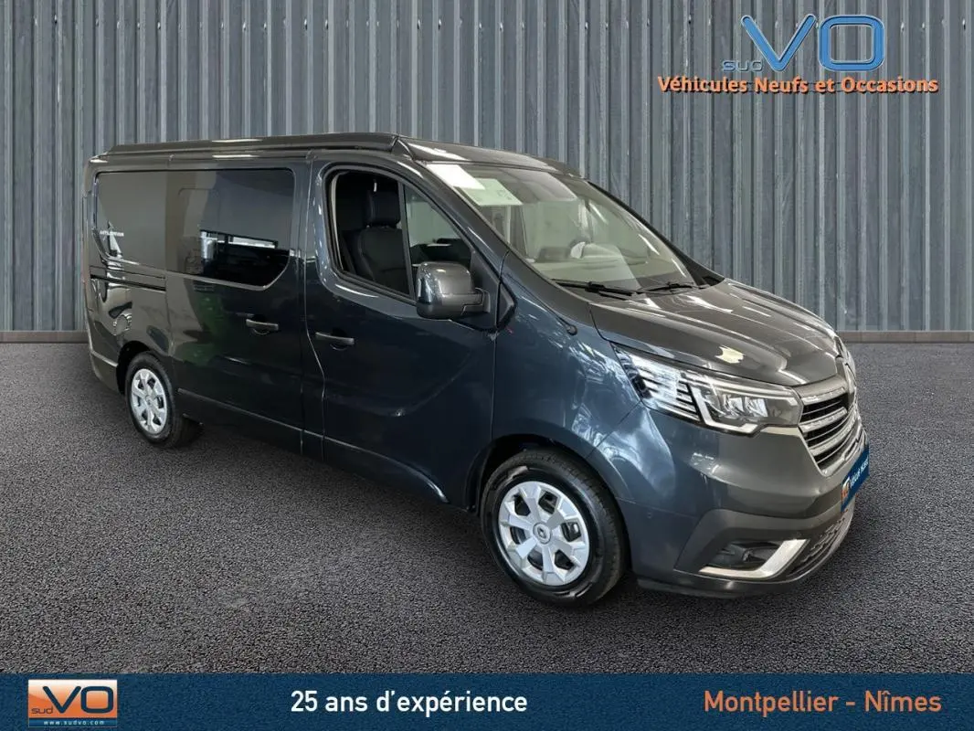Renault Trafic Fourgon gris en 3/4 avant droit, vitres surteintées et jantes alliage visibles en intérieur showroom.