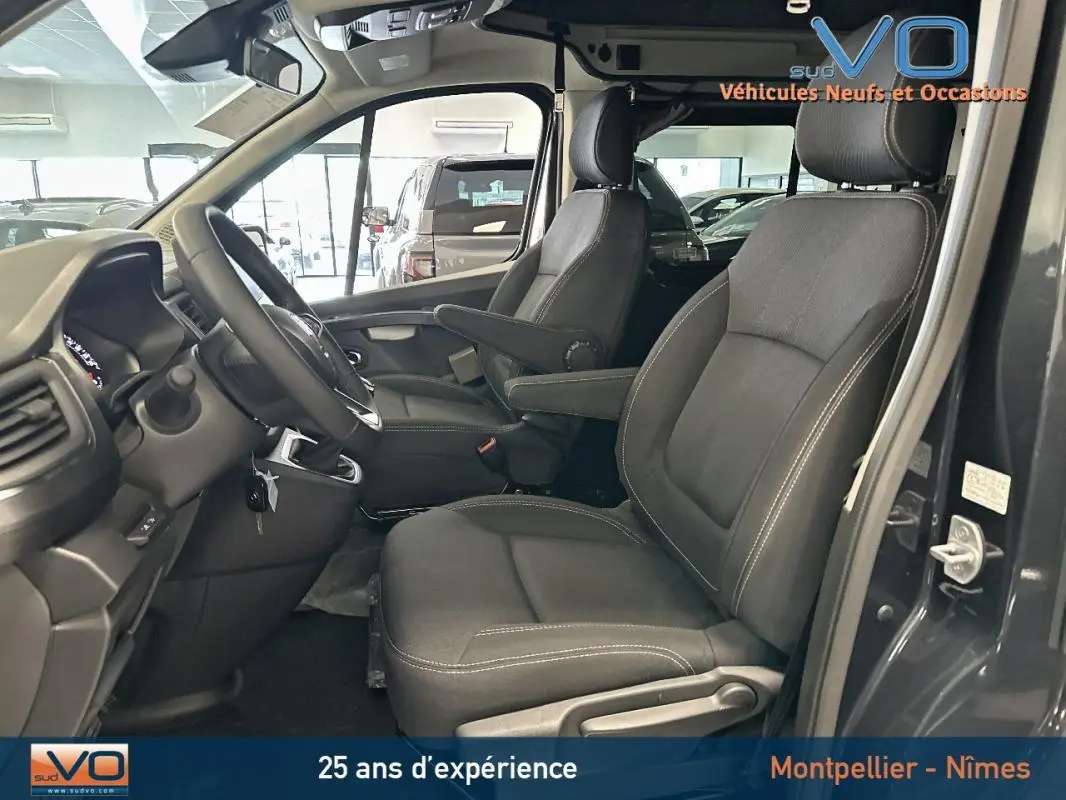 Vue intérieure côté conducteur du Renault Trafic Fourgon gris 2025, sièges confort avec accoudoirs et tableau de bord visible.