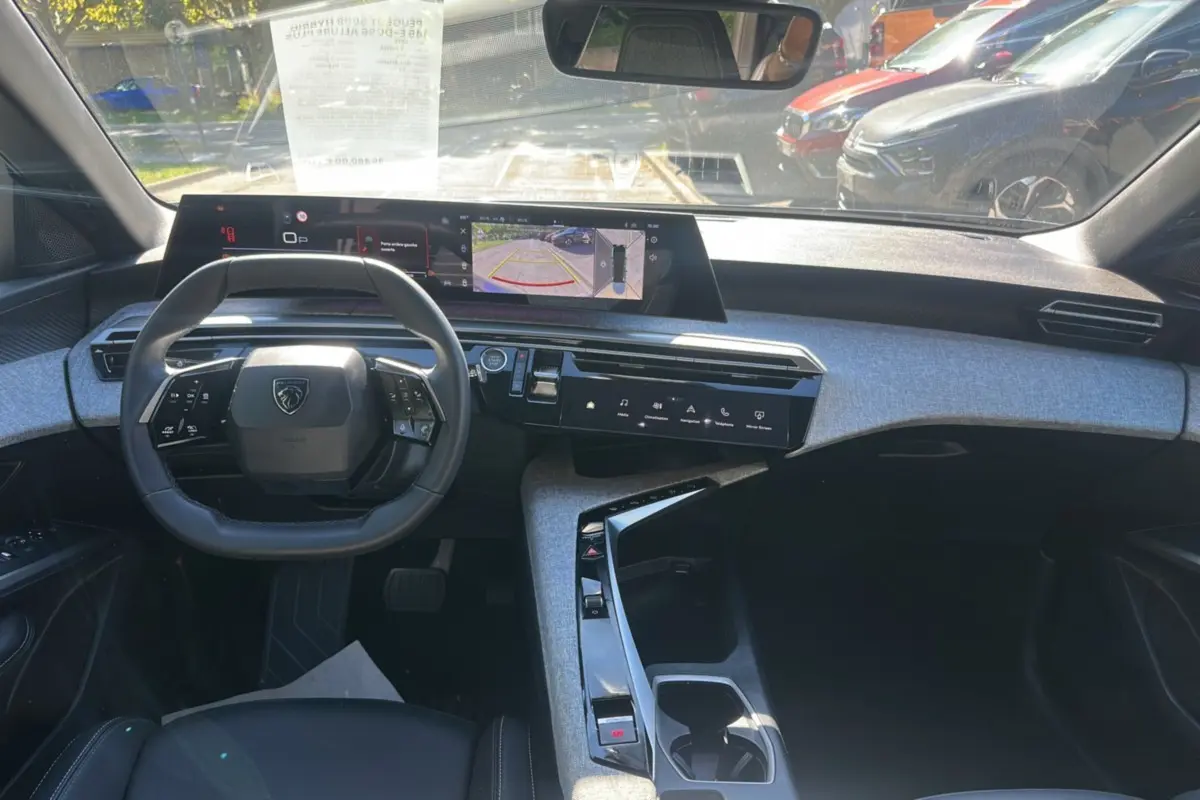 Vue intérieure avant du Peugeot 5008 Hybrid 145 gris artense, avec tableau de bord numérique panoramique et volant cuir multifonctions.
