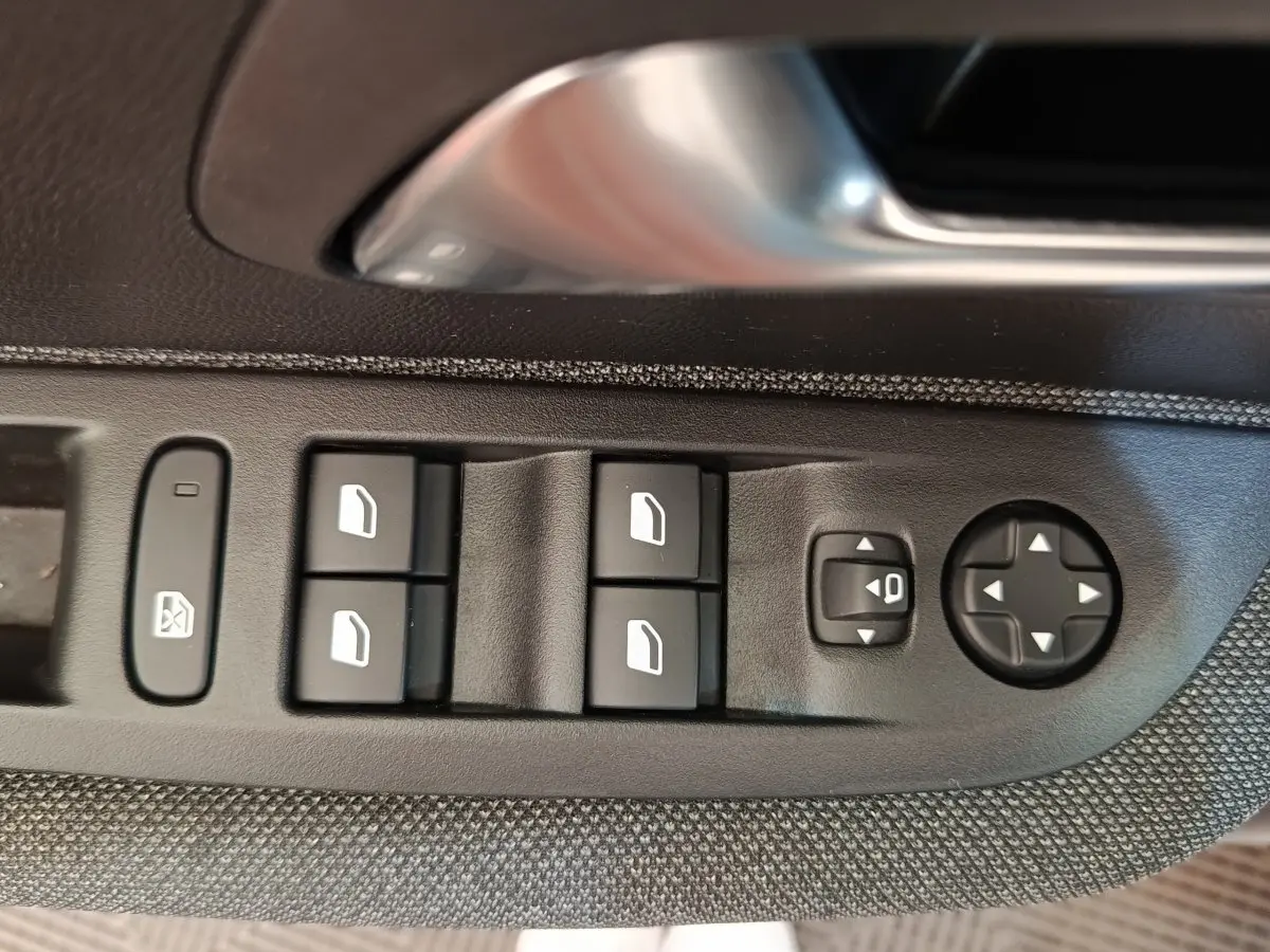 Gros plan sur les commandes des vitres et rétroviseurs côté conducteur d'une Peugeot 208 blanche de 2023.
