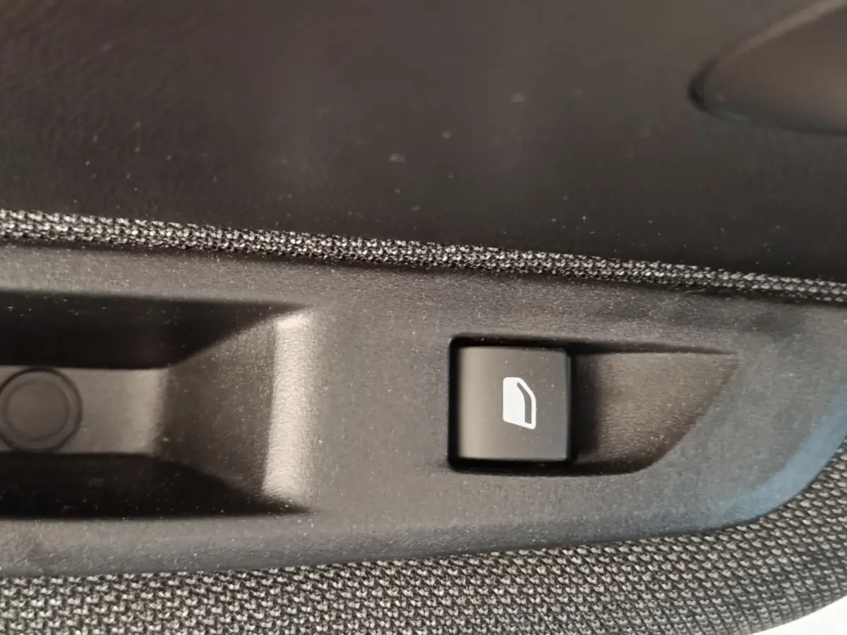 Gros plan sur le bouton d'ouverture de trappe à carburant noir dans l'habitacle d'une Peugeot 208 blanche 2023.