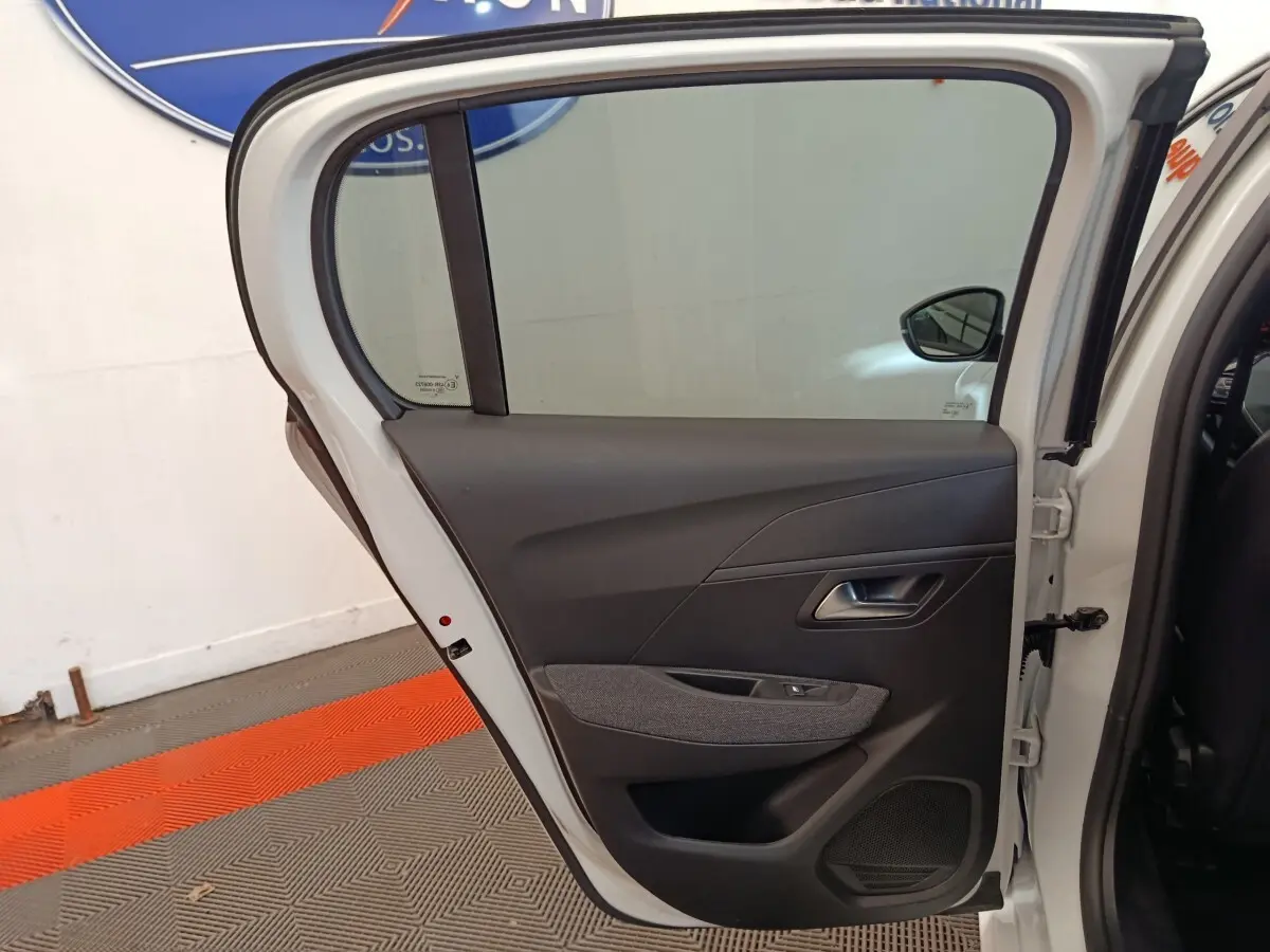 Vue intérieure de la porte arrière droite blanche d'une Peugeot 208 2023, avec garniture noire et tissu gris.