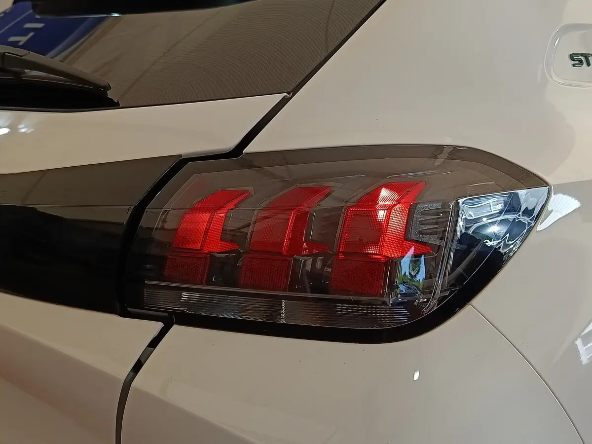 Gros plan sur le feu arrière droit rouge et noir de la Peugeot 208 blanche PureTech 75 S&S Style 2023.