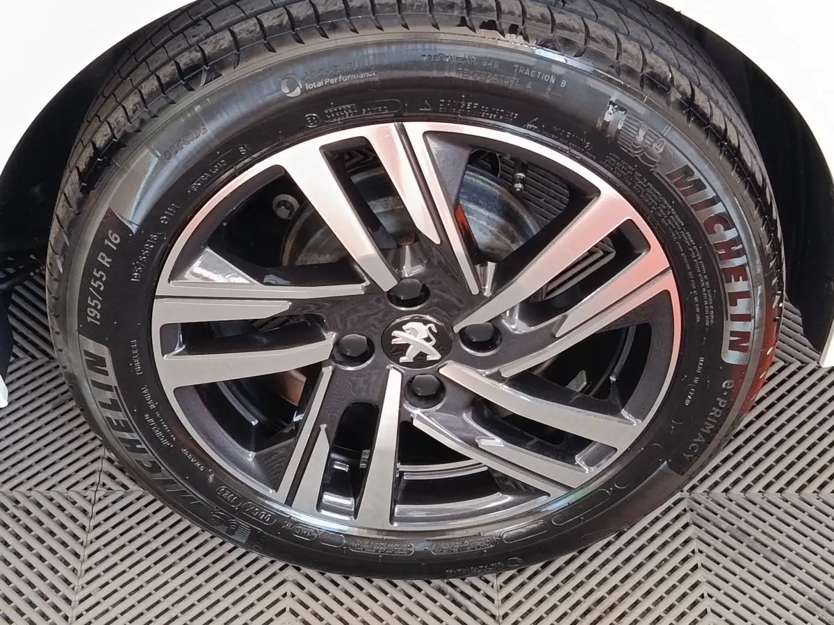 Gros plan sur la jante alliage bicolore avec logo Peugeot d'une 208 PureTech blanche, pneu Michelin visible.