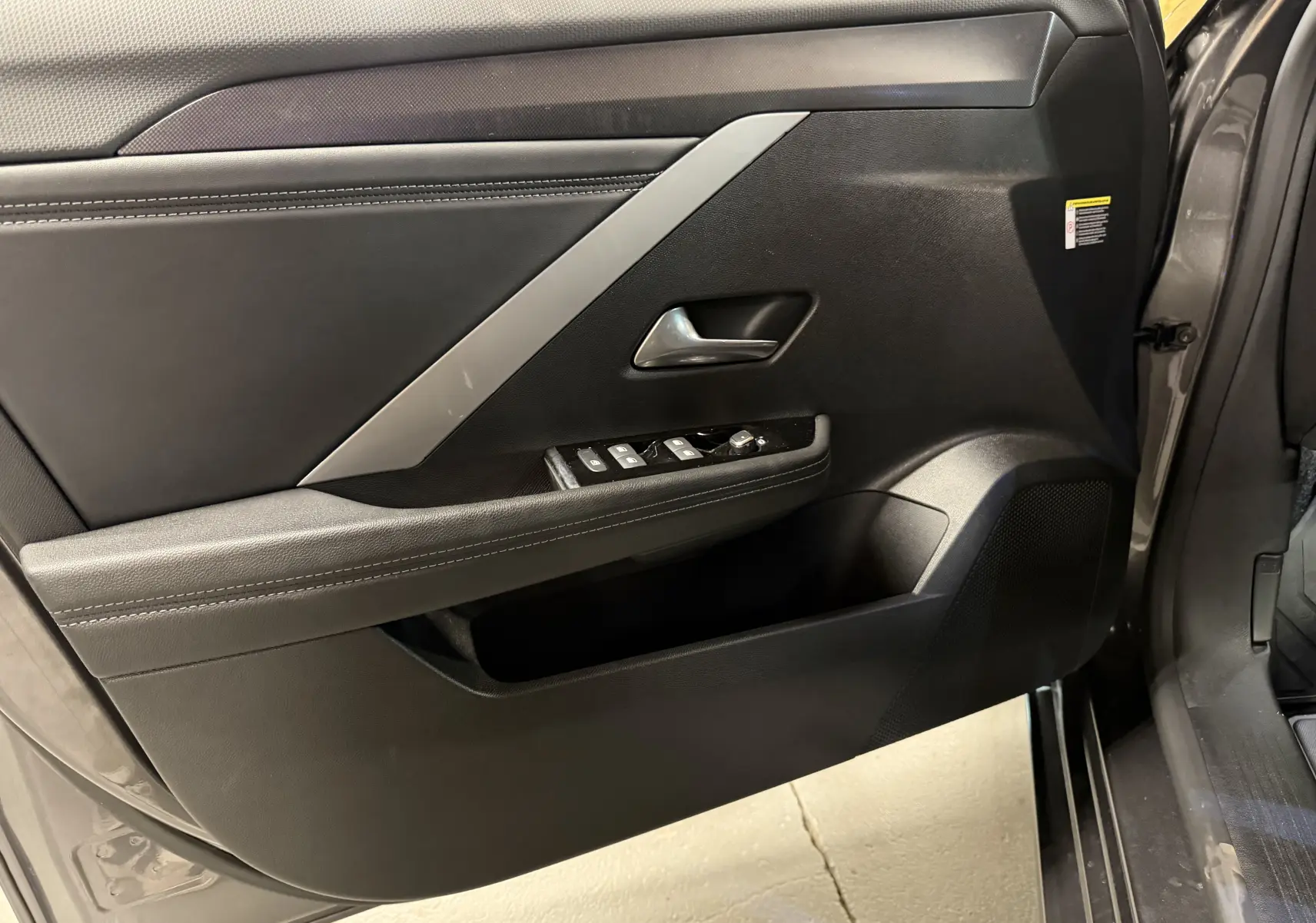 Vue intérieure de la porte avant gauche grise de l'Opel Astra 2024 avec commandes de vitres et accoudoir en cuir noir.