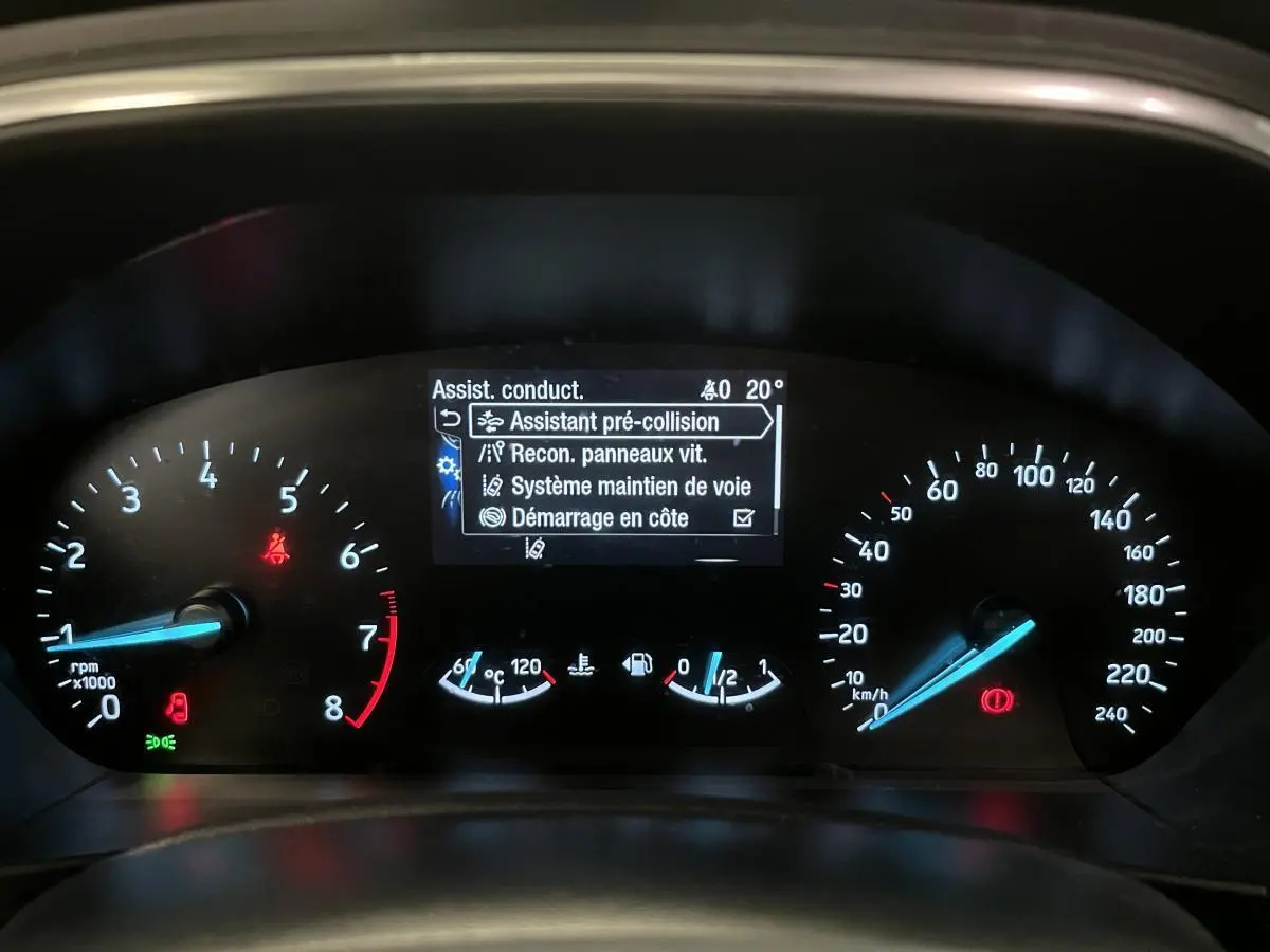 Tableau de bord de Ford Focus gris 2021 montrant l'écran d'assistance à la conduite et compteurs analogiques.