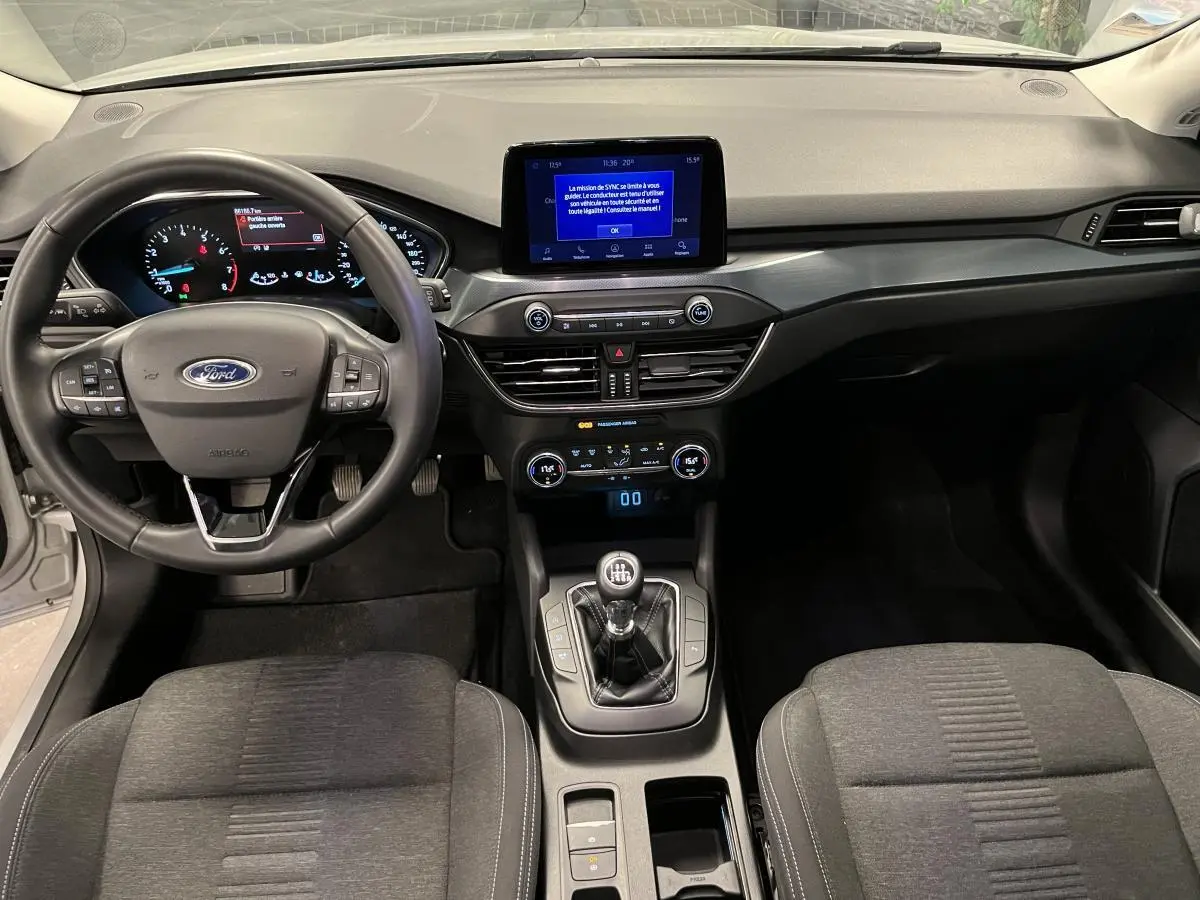 Vue intérieure avant de la Ford Focus 1.0 EcoBoost 2021 avec tableau de bord noir et console centrale équipée d'une boîte manuelle.
