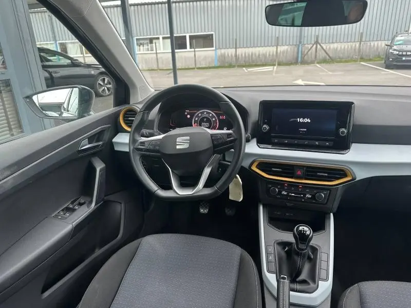 Vue intérieure avant du SEAT Arona 2025 avec volant multifonction, tableau de bord numérique et touches jaunes autour des aérateurs.