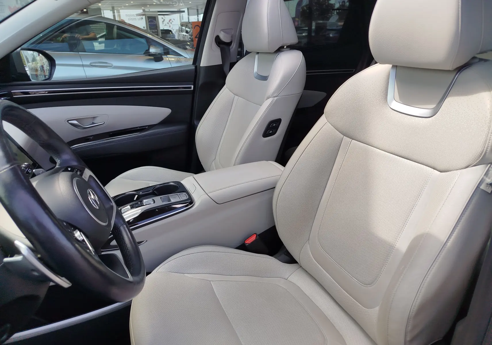 Vue intérieure côté conducteur du Hyundai Tucson 2021, sièges cuir beige clair avec console centrale et volant visibles.