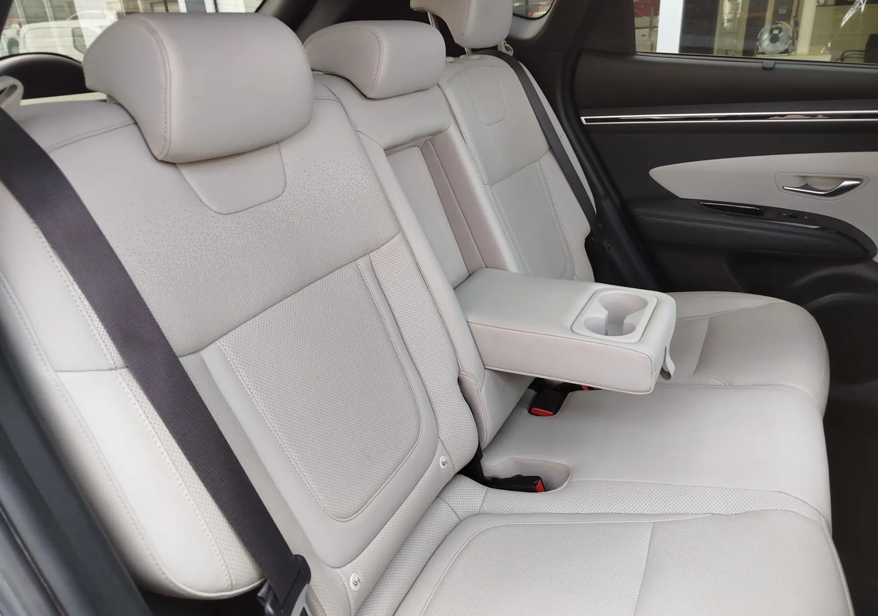 Vue intérieure côté droit des sièges arrière en cuir beige clair du Hyundai Tucson 2021 avec accoudoir central rabattable et porte-gobelets.