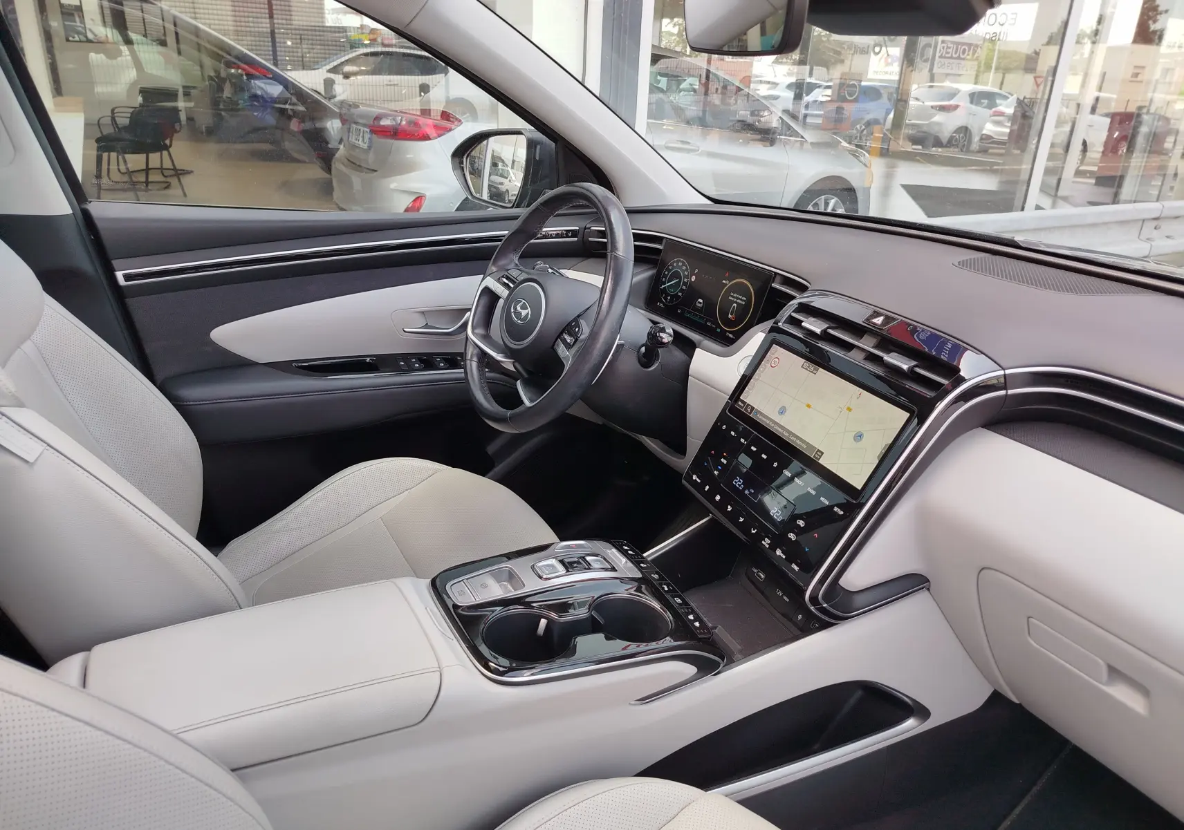 Vue intérieure côté conducteur du Hyundai Tucson 2021, avec sièges cuir clairs et tableau de bord moderne à écran tactile.