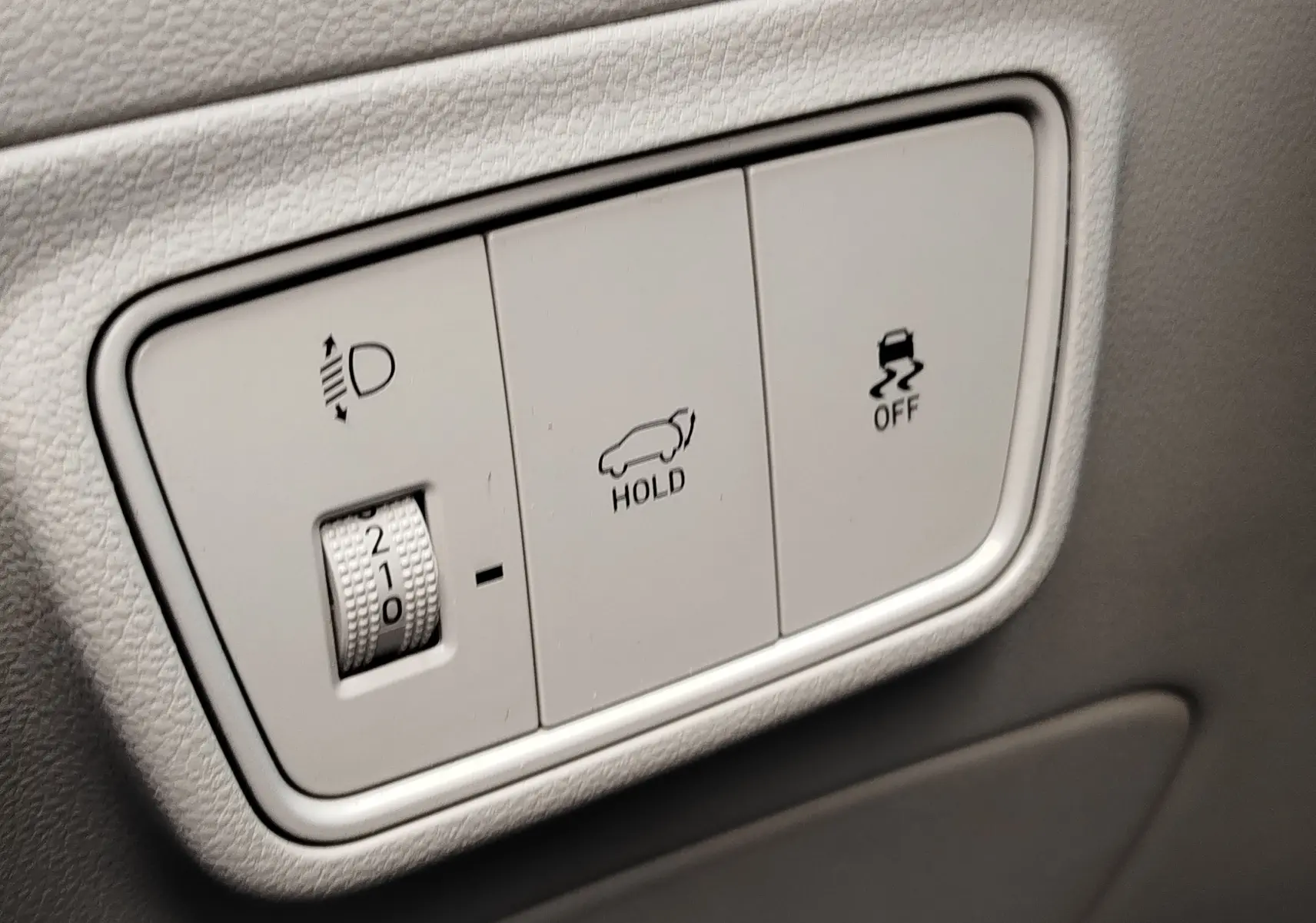 Gros plan sur les commandes intérieures blanches du Hyundai Tucson 1.6 CRDI 136ch Hybride, avec réglage des phares et fonctions hold et traction.