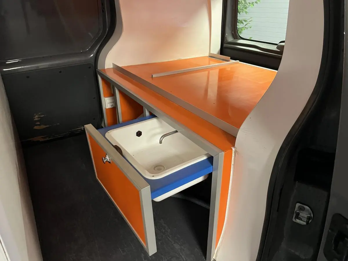 Vue intérieure côté gauche du Renault Kangoo Express 2016, montrant un meuble orange avec évier intégré dans l'espace de chargement.