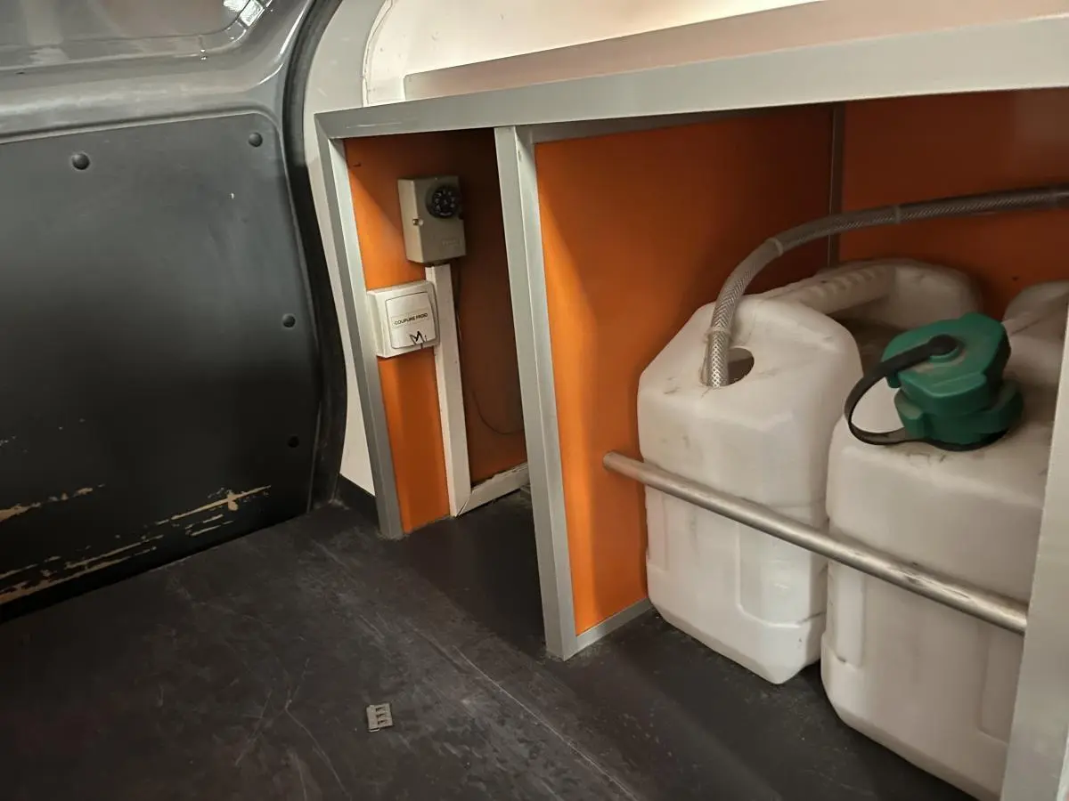 Détail intérieur du compartiment de chargement du Renault Kangoo Express gris foncé avec rangements et bidons blancs.