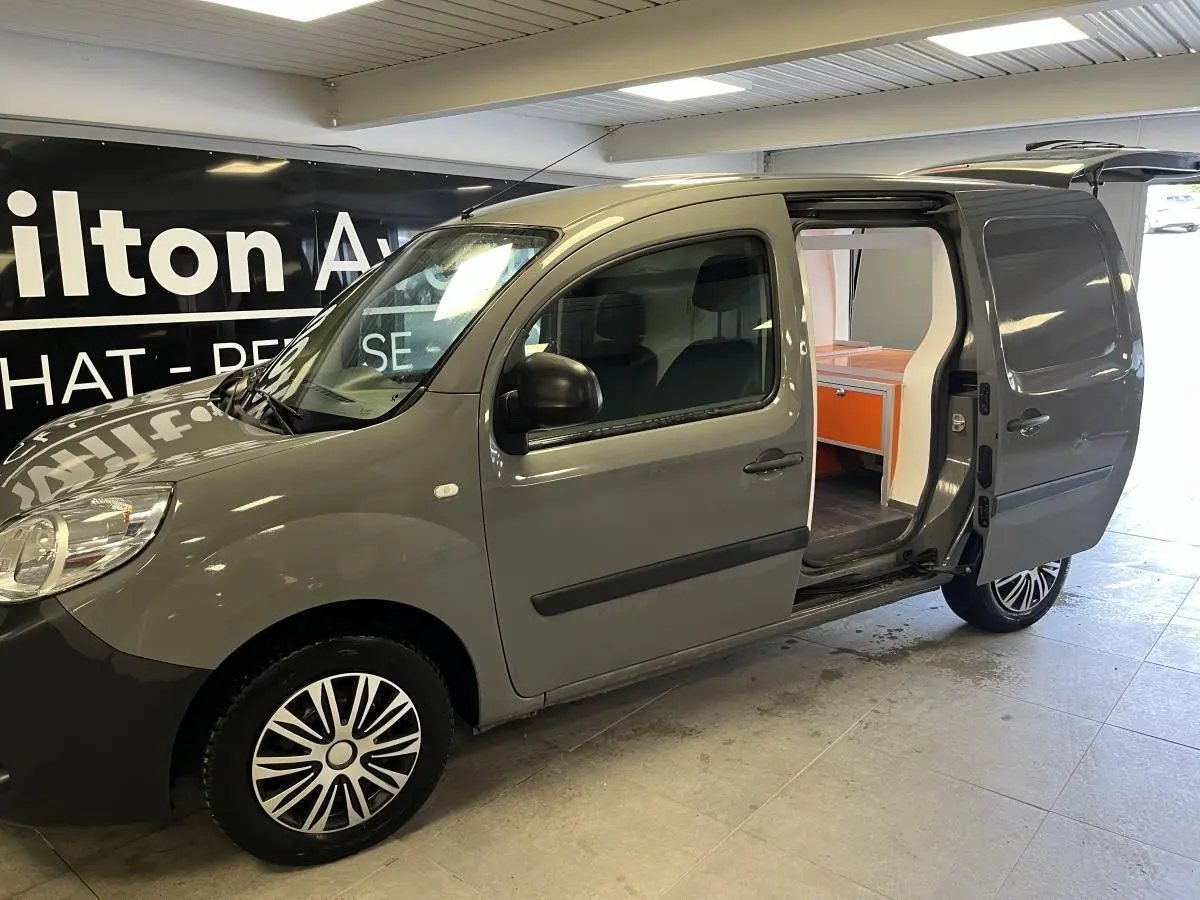 Vue 3/4 avant droit du Renault Kangoo Express gris foncé avec porte latérale droite ouverte montrant l'espace de chargement aménagé.