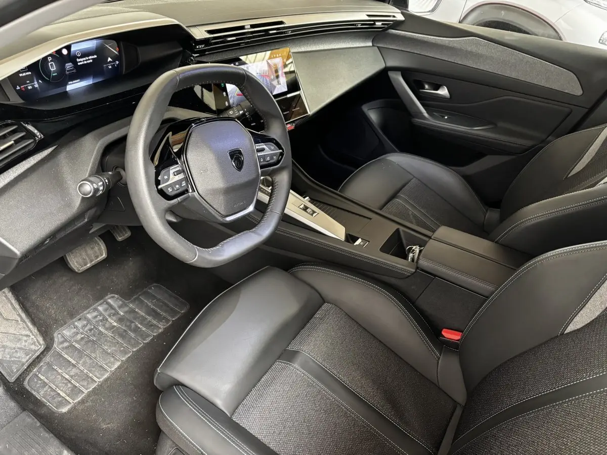 Intérieur noir de la Peugeot 308 PureTech 130 S&S Allure 2024, vue côté conducteur avec tableau de bord digital et volant cuir.